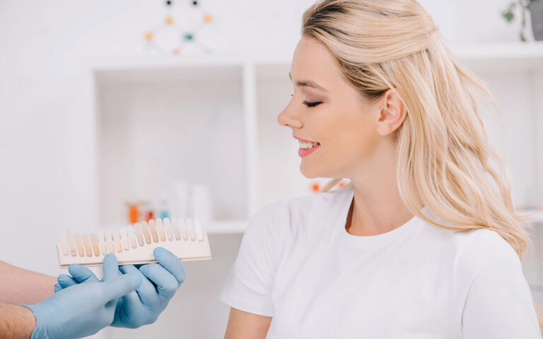 Beautiful woman looking at dentist holding teeth color palette