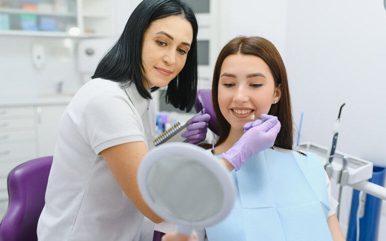Young woman choosing color of teeth at dentist